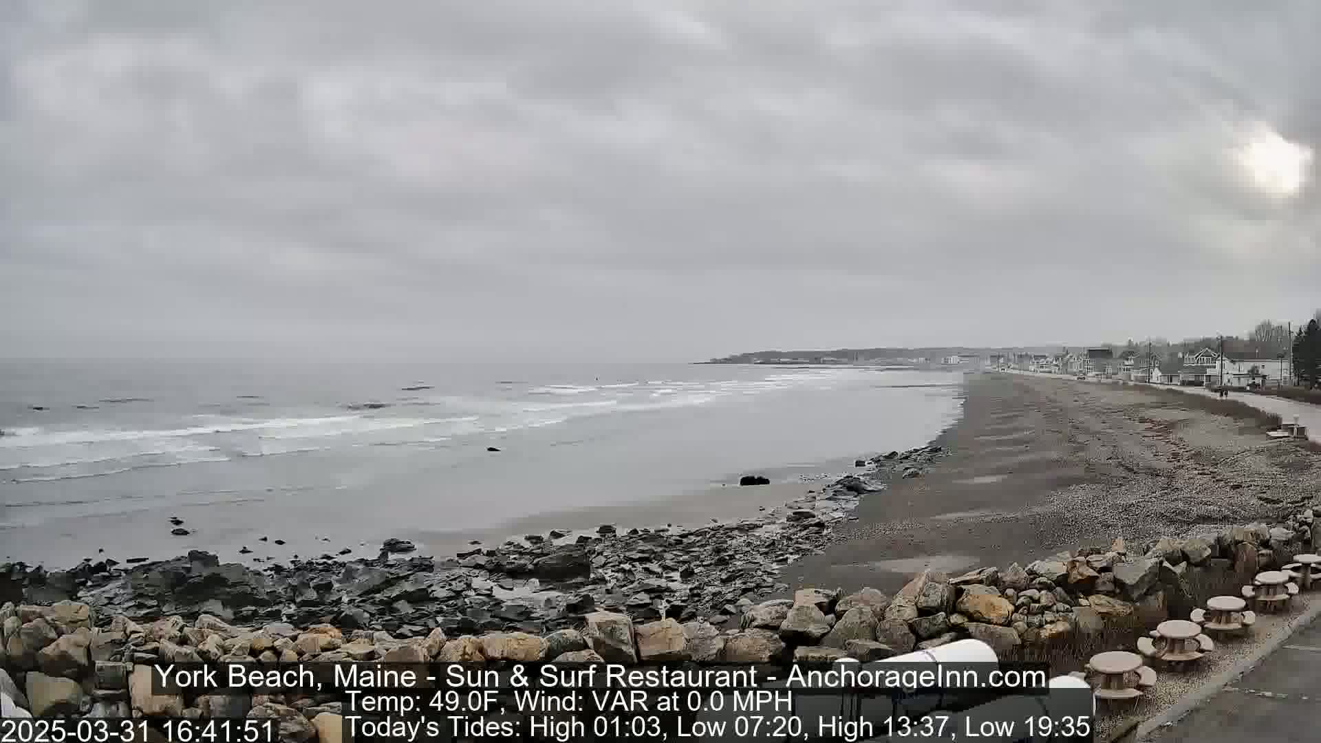 A rocky beach stretches along a calm, gray ocean under an overcast sky.