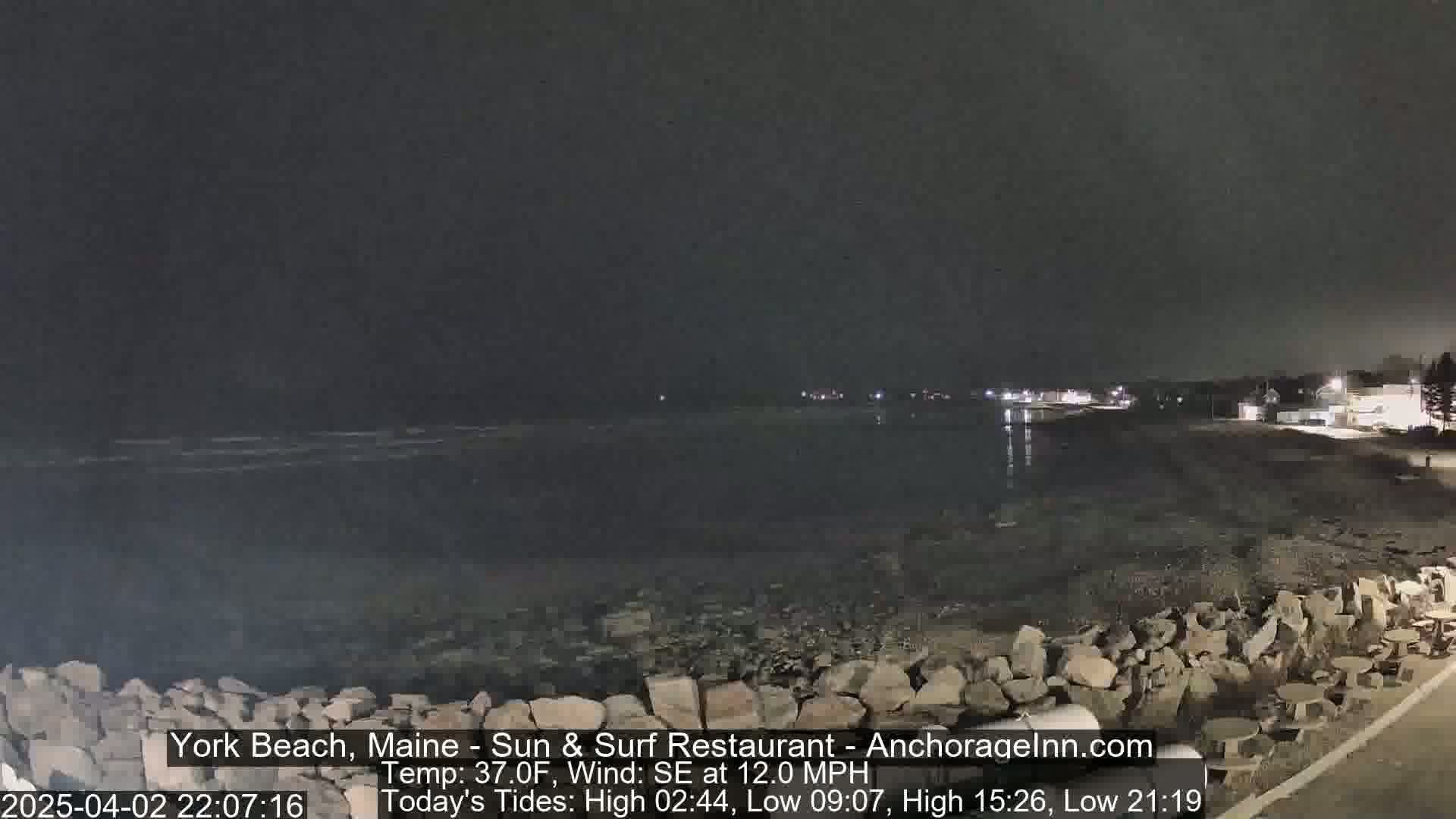 A nighttime view of a rocky shoreline and calm ocean under a dark sky.