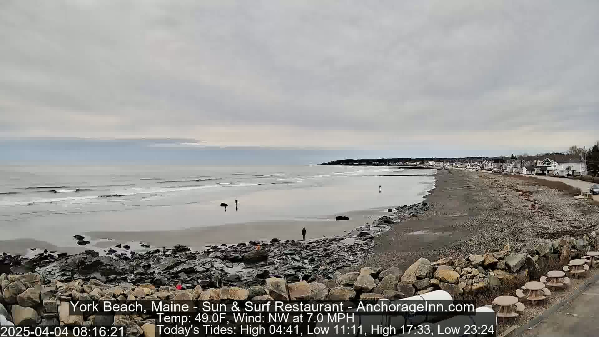 A wide, rocky beach stretches out to a calm, gray ocean under an overcast sky.