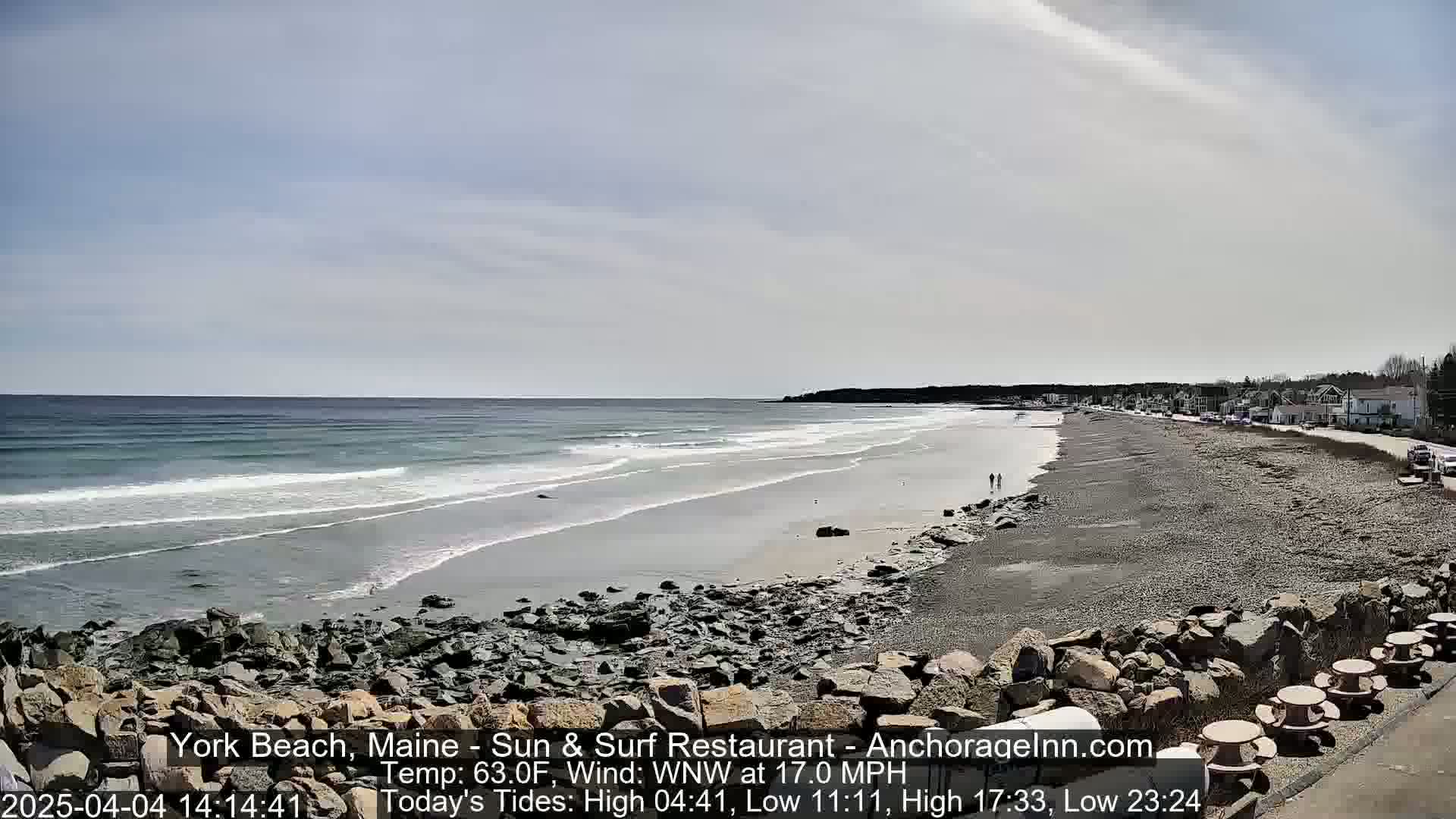 A rocky shoreline with a sandy beach stretches along a calm ocean under a partly cloudy sky.