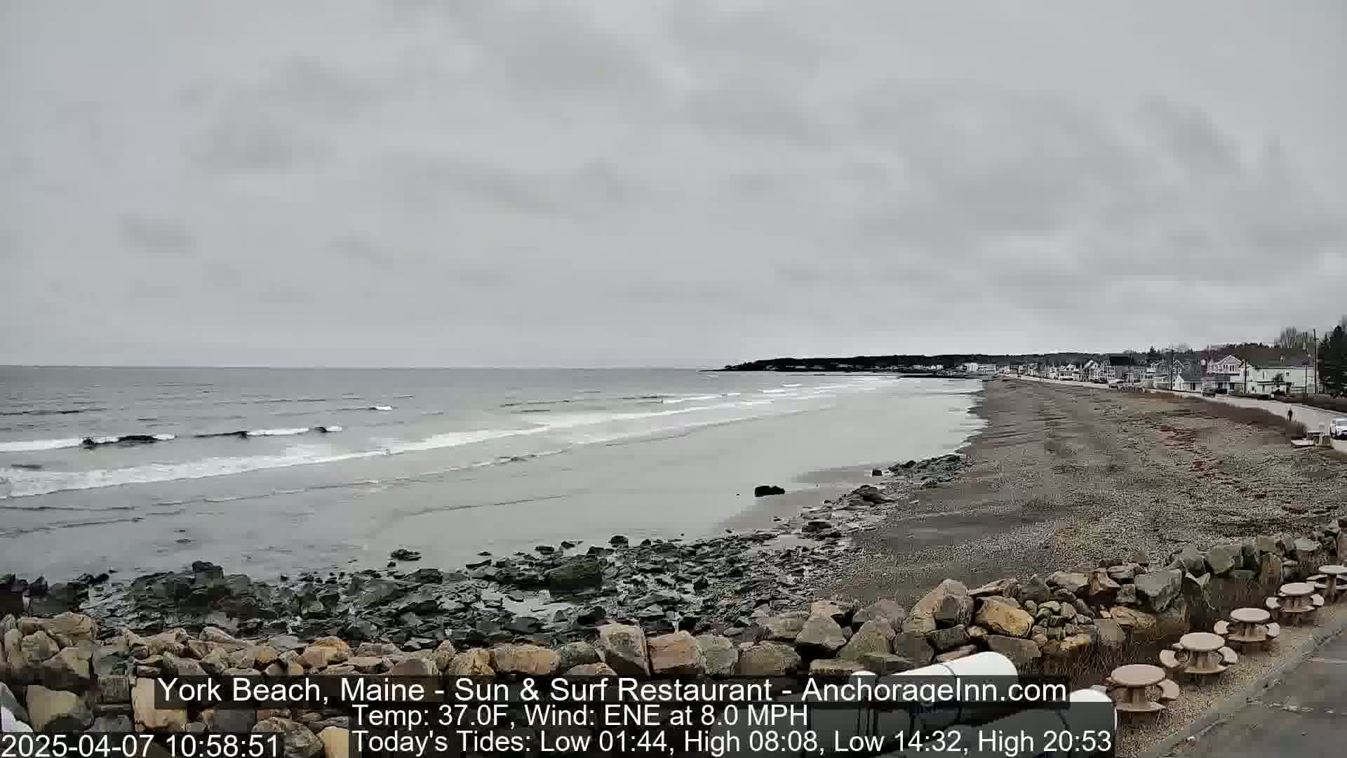 A rocky beach with small waves under an overcast sky, showing a town in the distance.