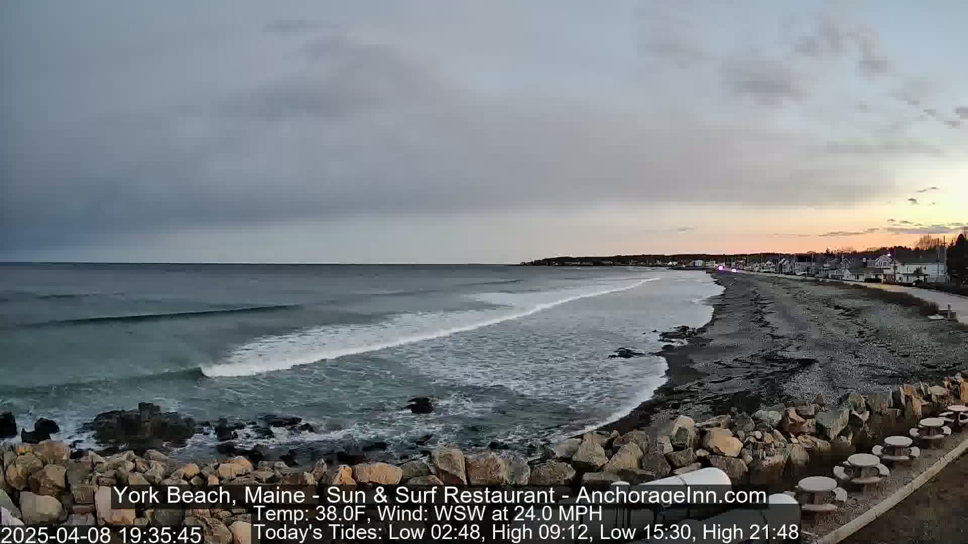 A rocky beach with waves rolling in under an overcast sky at sunset.