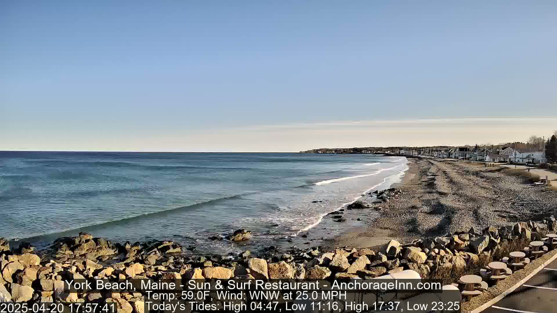 A rocky beach with gentle waves under a clear blue sky, and a small town visible in the distance.