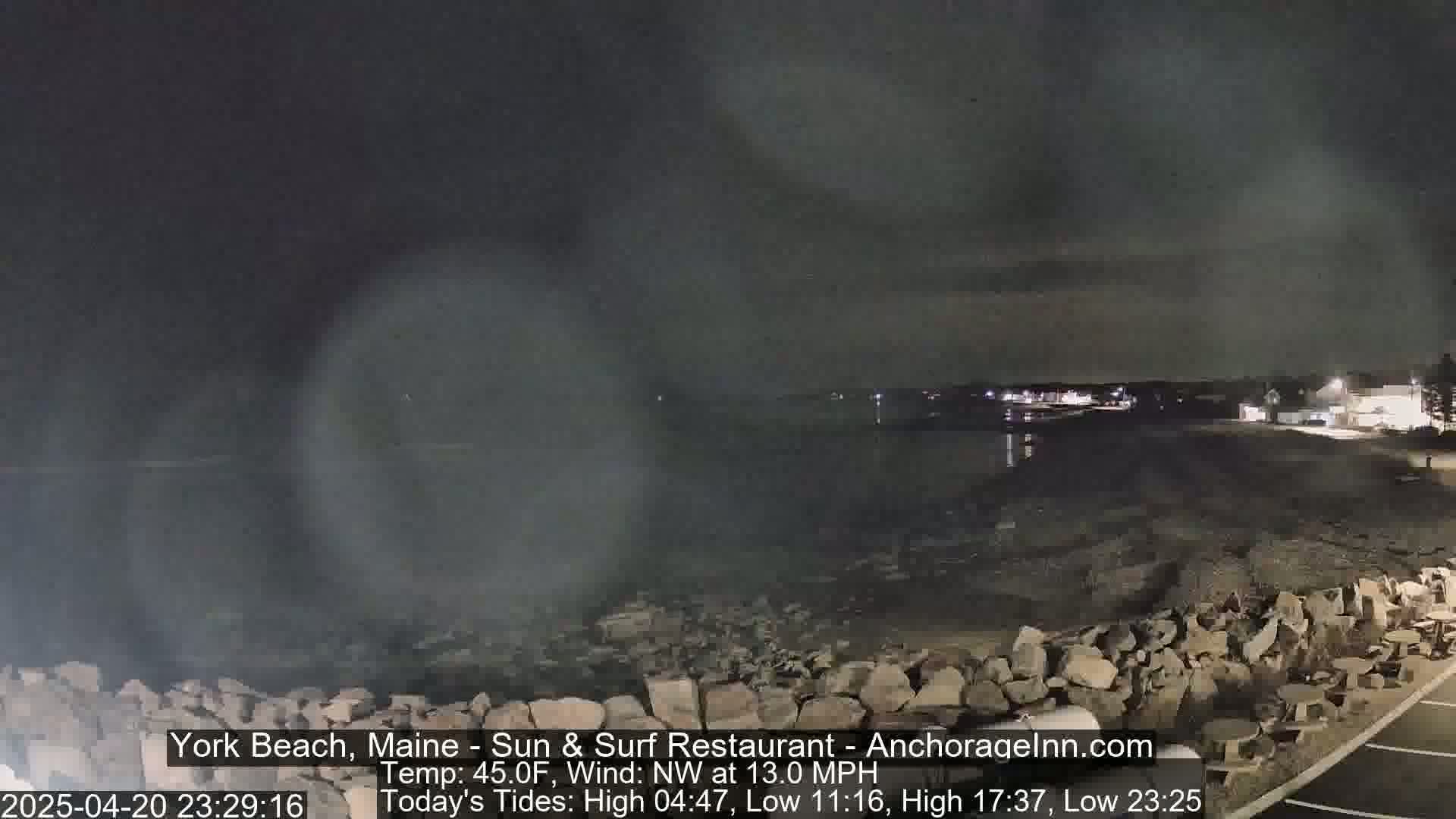 A nighttime view of a rocky shoreline and calm water under a dark, cloudy sky.