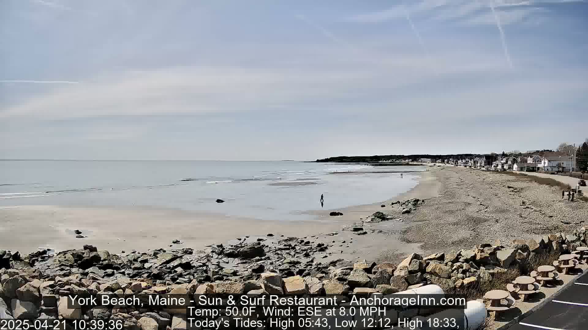 A sandy beach with rocky areas stretches to a calm ocean under a partly cloudy sky.