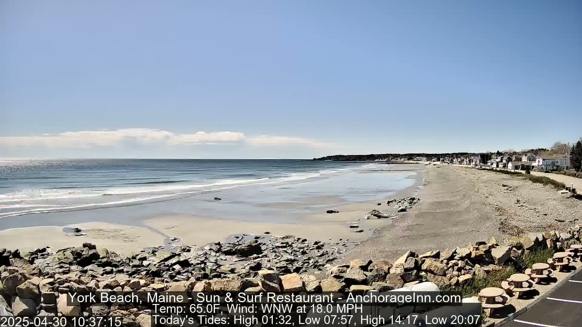 A sandy beach with rocky outcrops and small waves under a partly cloudy sky.