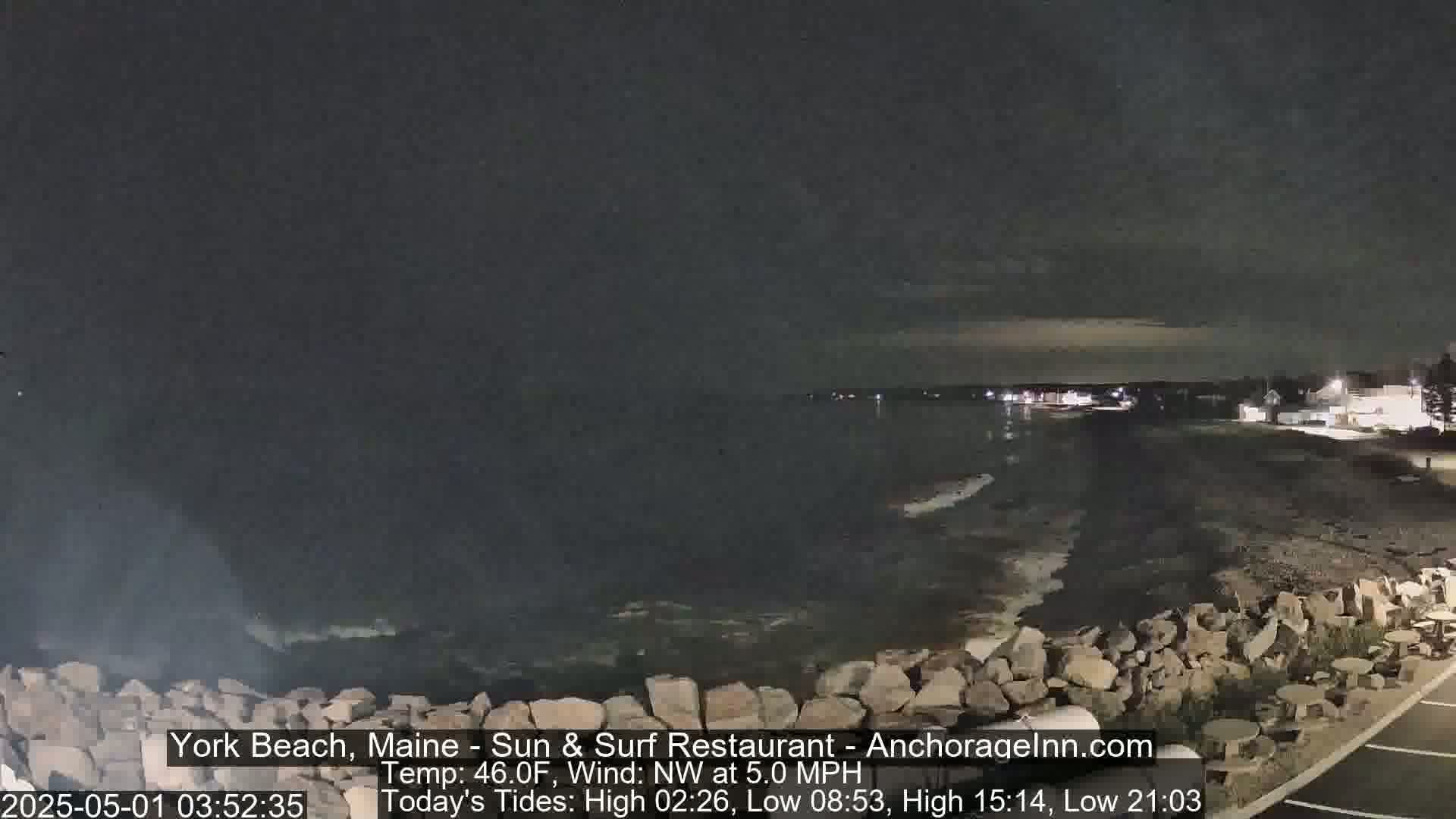 A nighttime view of a rocky shoreline and calm ocean under a dark sky.
