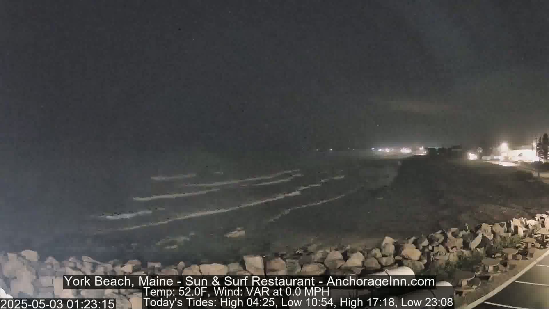 A nighttime view of a rocky shoreline with calm ocean waves under a dark sky.