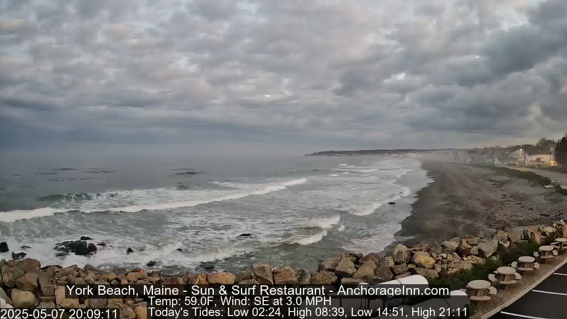 A rocky shoreline with small waves crashing on a beach under a cloudy sky.