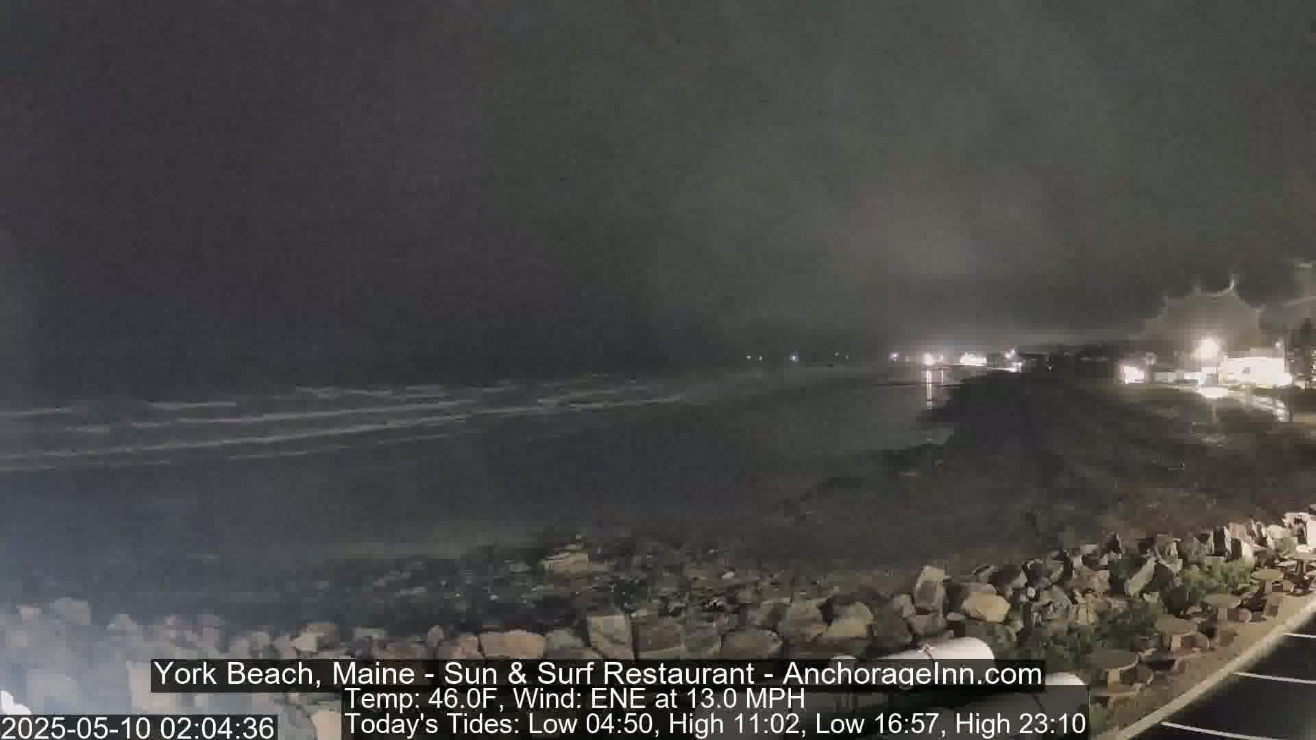 A nighttime view of a rocky shoreline and dark, wavy ocean under a cloudy sky.