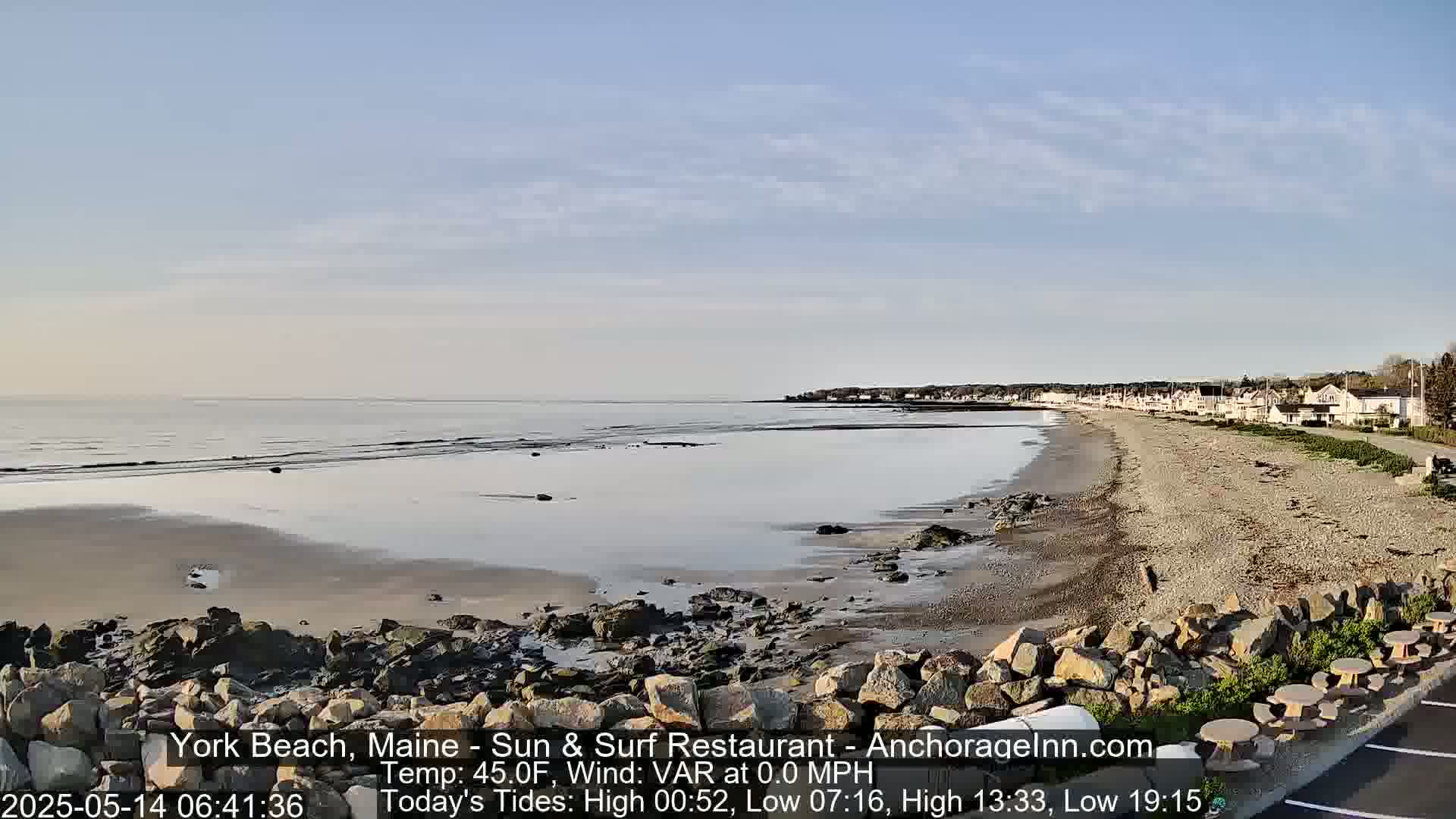 A calm, sandy beach stretches out to a quiet ocean under a clear, pale blue sky.