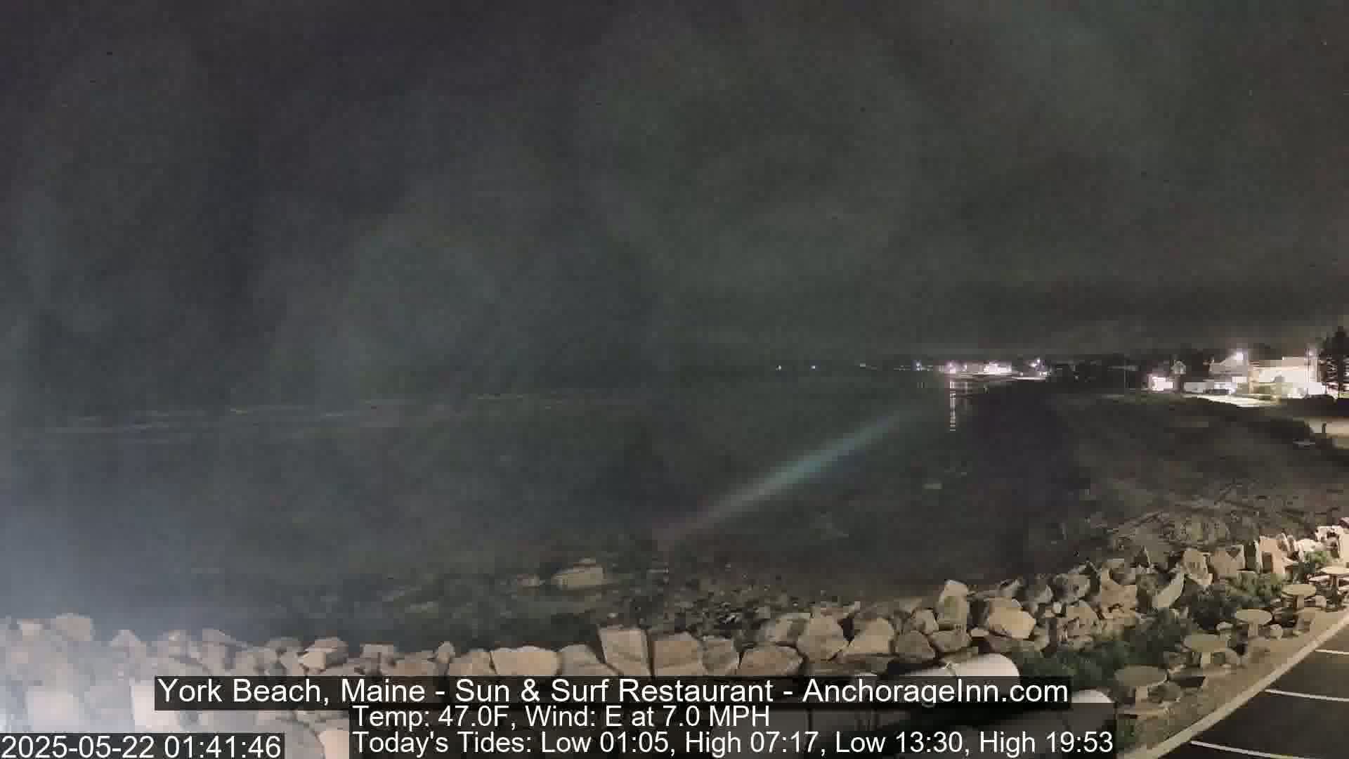 A nighttime view of a rocky shoreline and calm water under a dark, cloudy sky.