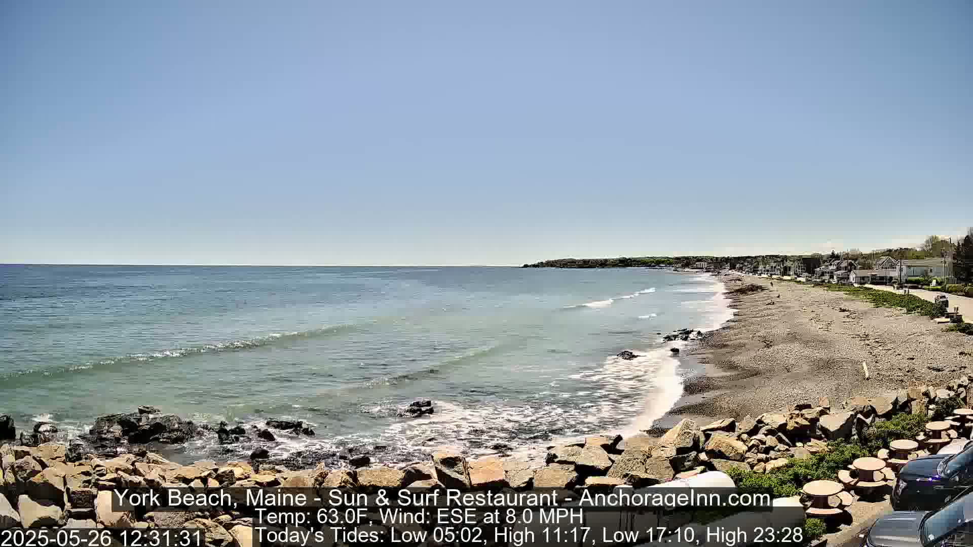 A rocky beach with gentle waves laps a shoreline under a clear blue sky.