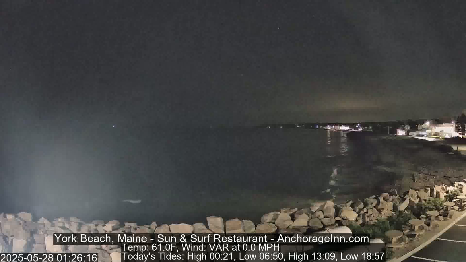 A nighttime view of a rocky shoreline and calm ocean under a dark sky.
