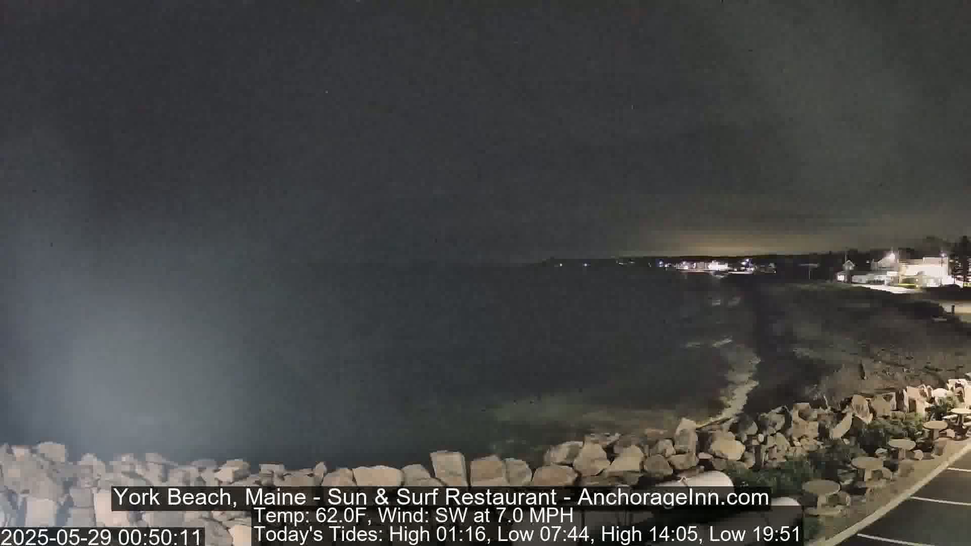 A nighttime view of a rocky shoreline with a calm ocean, under a dark sky.