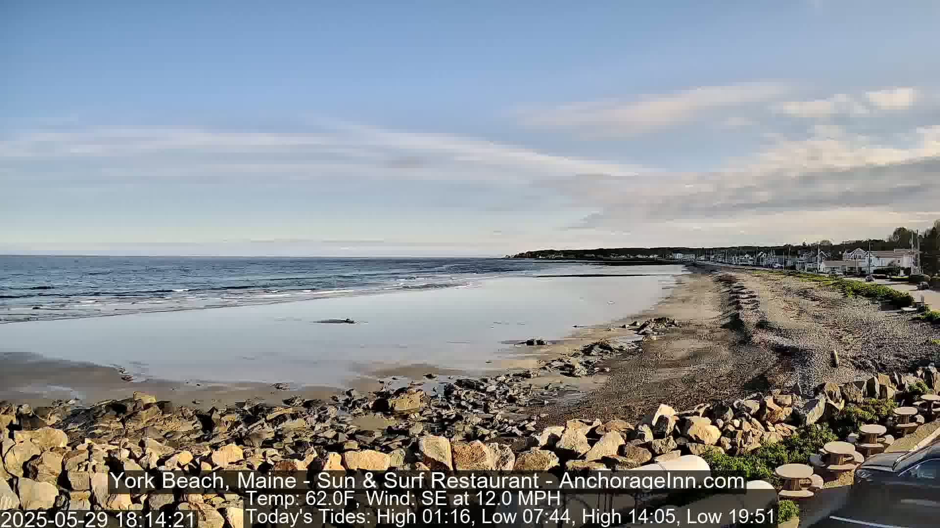 A sandy beach with rocky outcroppings stretches along a calm ocean under a partly cloudy sky.