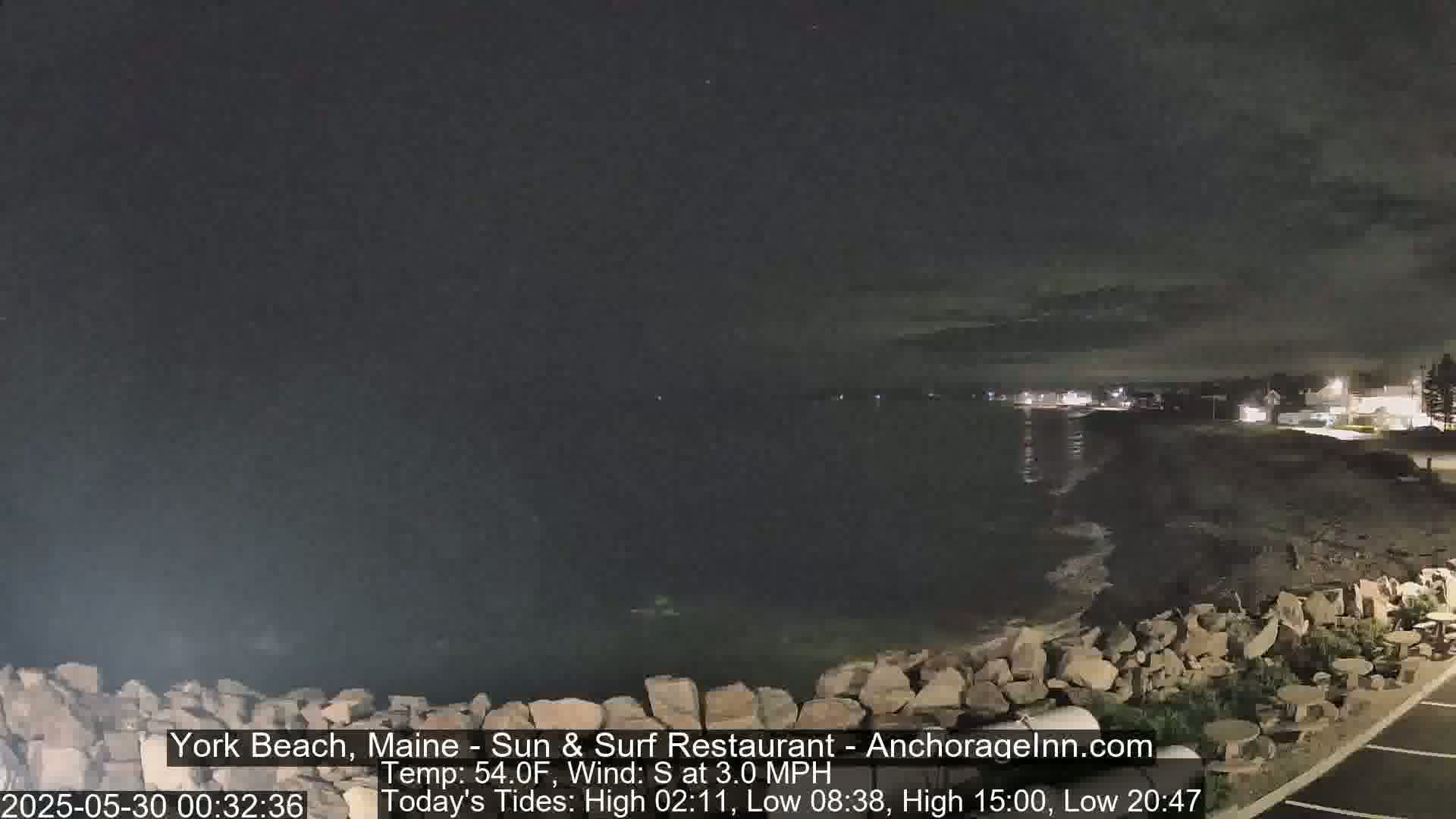 A nighttime view of a rocky shoreline with calm water under a dark, cloudy sky.