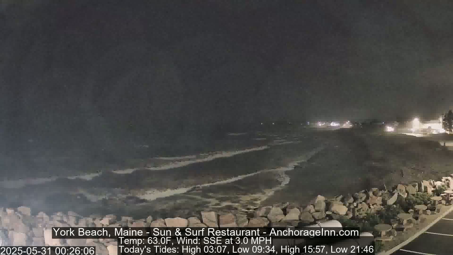 A nighttime view of a rocky shoreline with dark, gently lapping waves under a mostly clear sky.