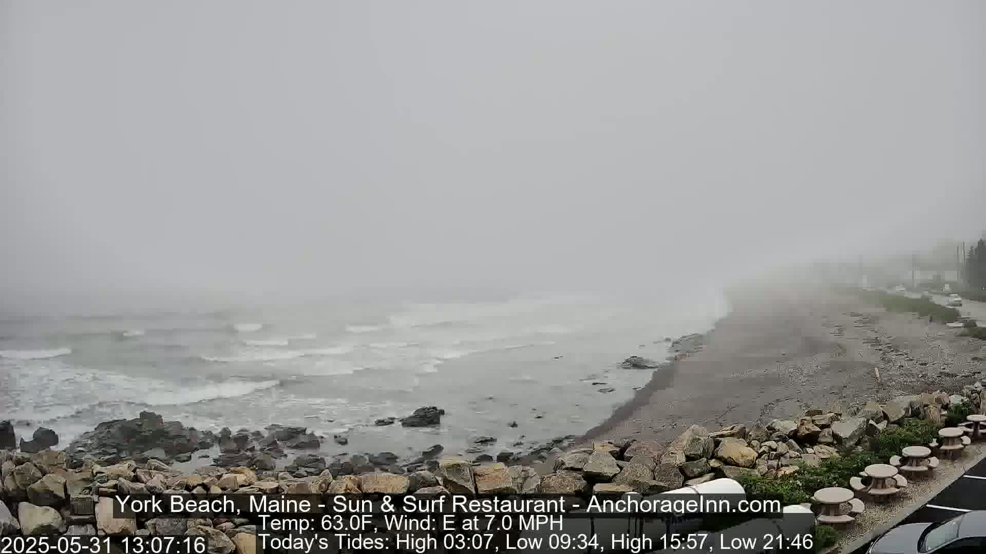 A rocky beach with moderate waves is shrouded in dense fog on an overcast day.