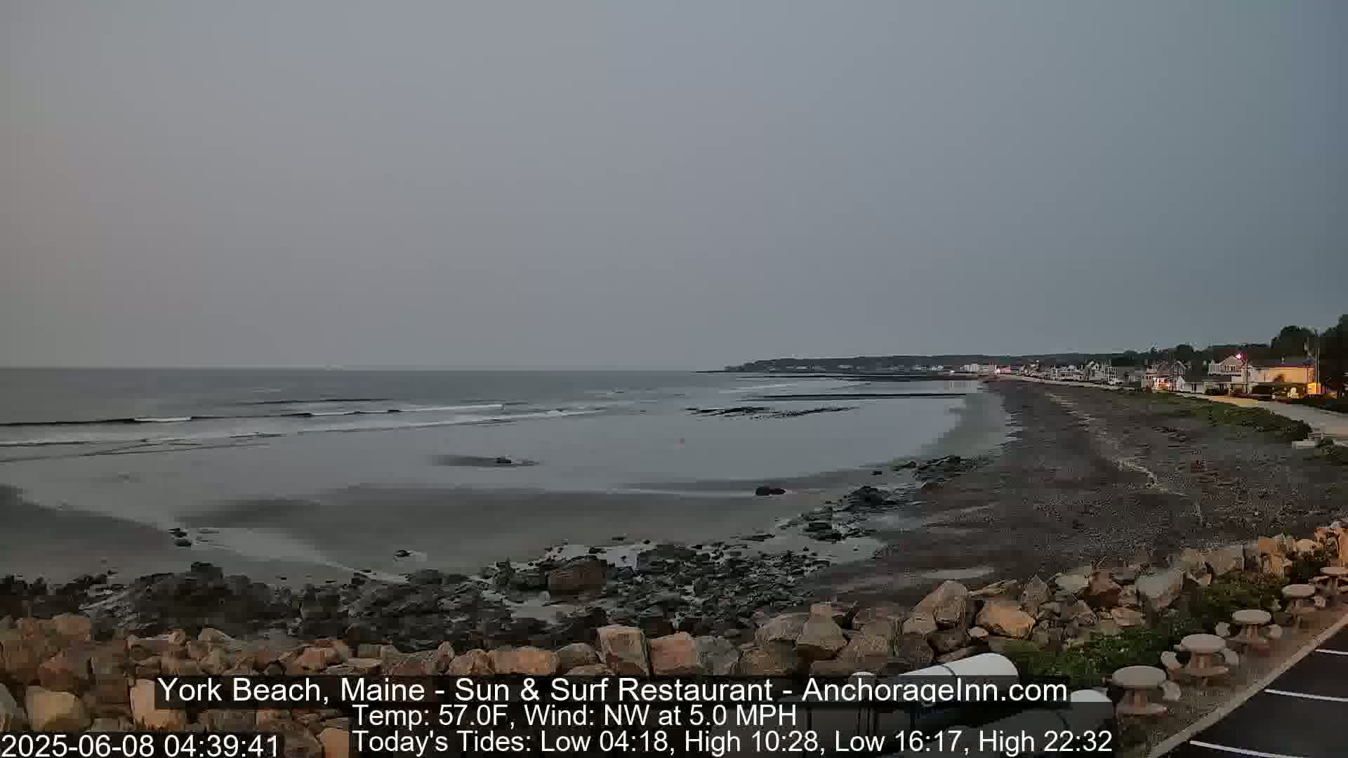 A rocky beach stretches along a calm, grey ocean under an overcast sky.