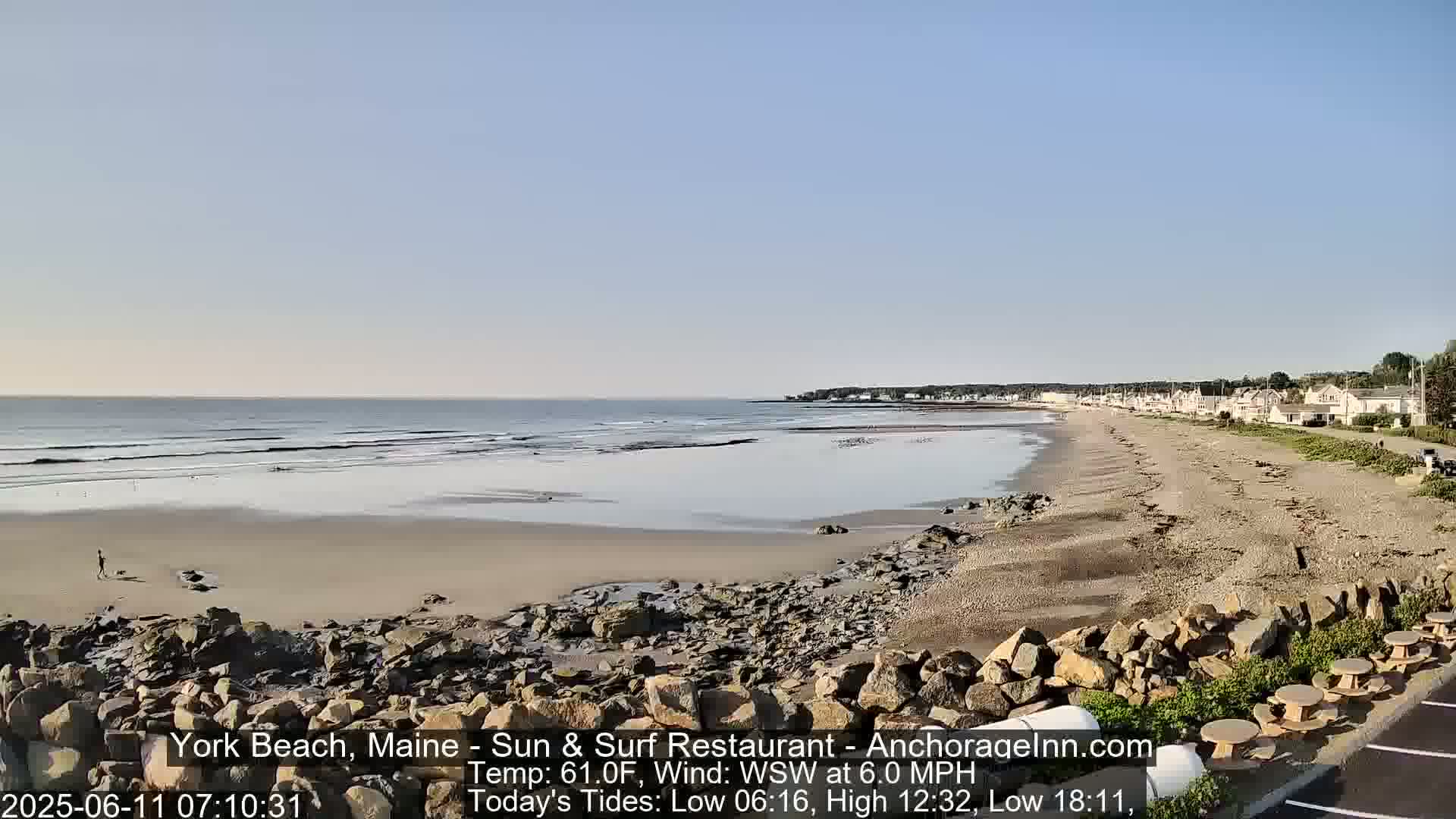 A sandy beach stretches along a calm ocean under a clear, bright sky, with a small town visible in the distance.