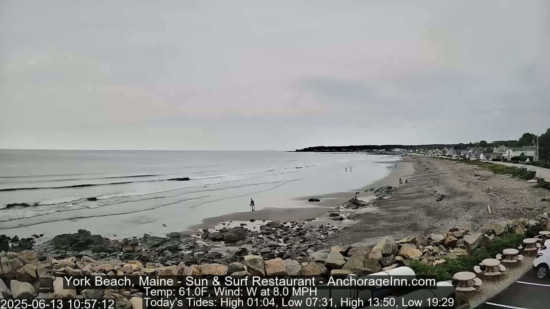 A rocky beach stretches along a calm, gray ocean under an overcast sky.