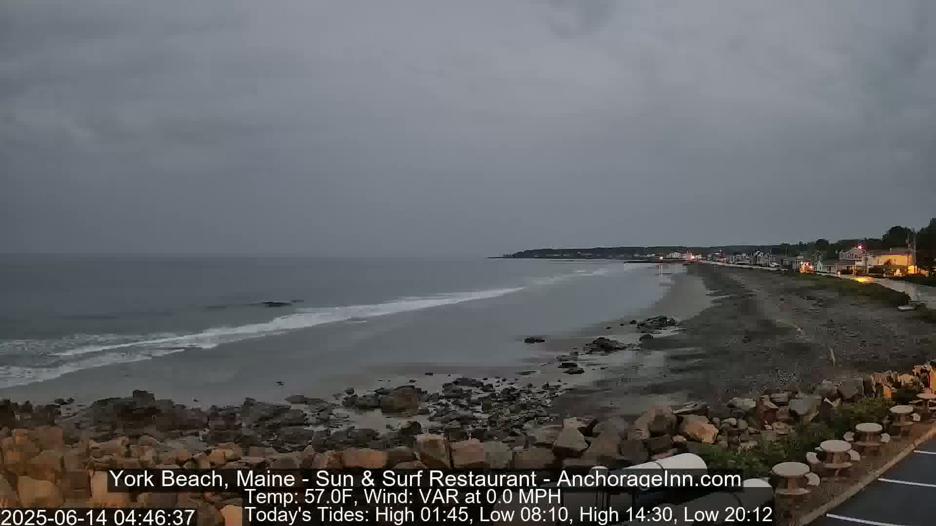 A rocky shoreline with a calm ocean under an overcast sky is visible at dawn.