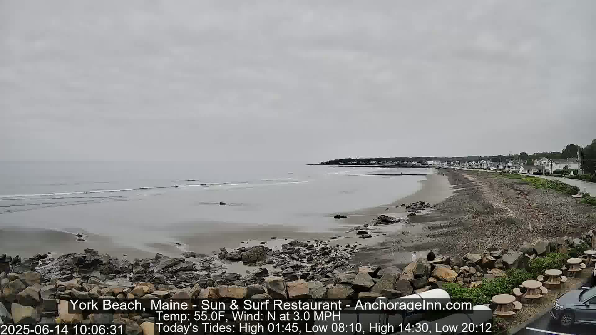 A rocky beach stretches along a calm, gray ocean under an overcast sky.