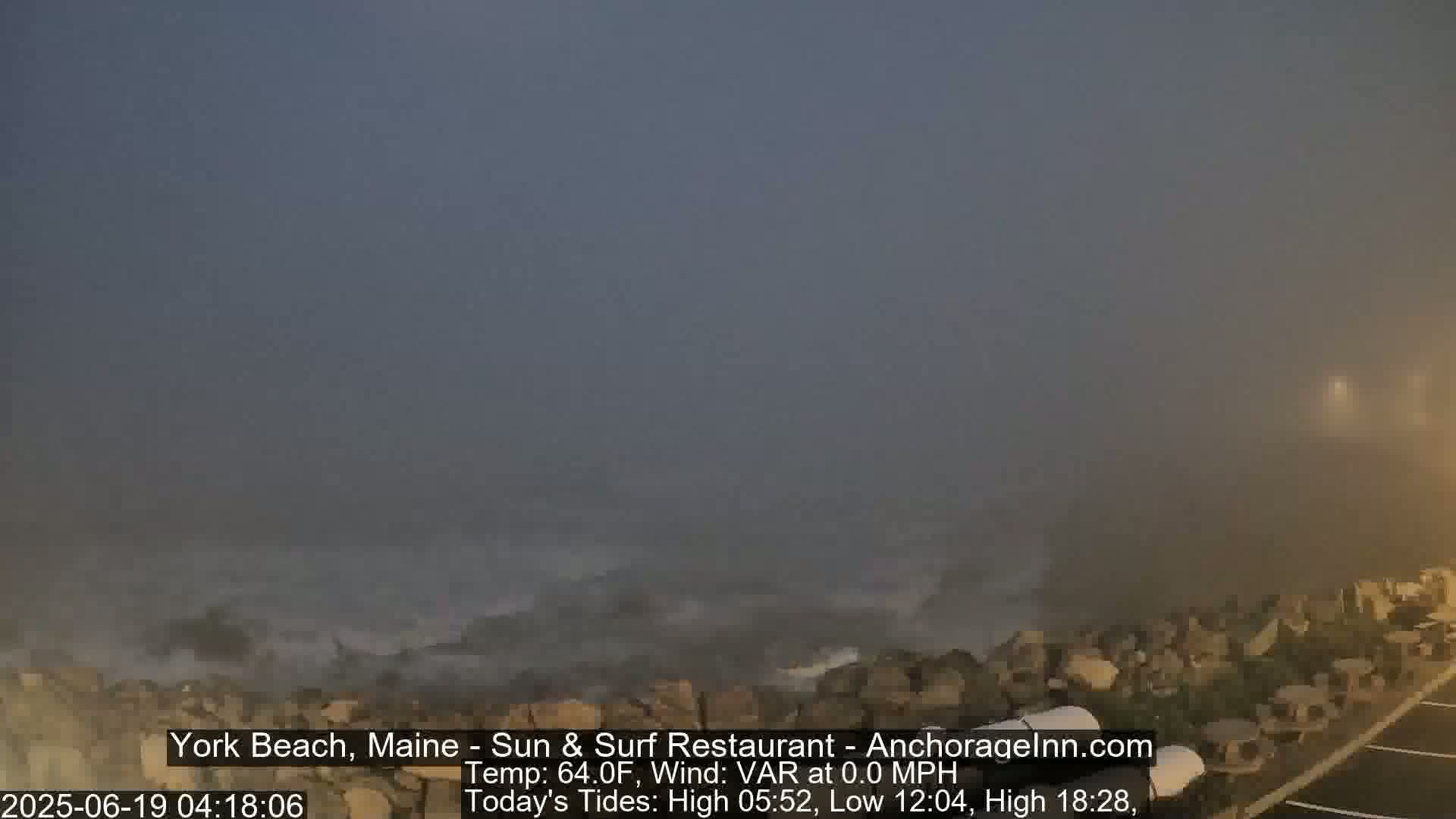 A foggy coastal scene shows waves crashing against a rocky shore.
