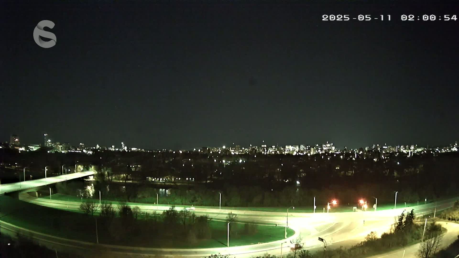 A nighttime view of a highway interchange with a city skyline in the distance under a clear, dark sky.