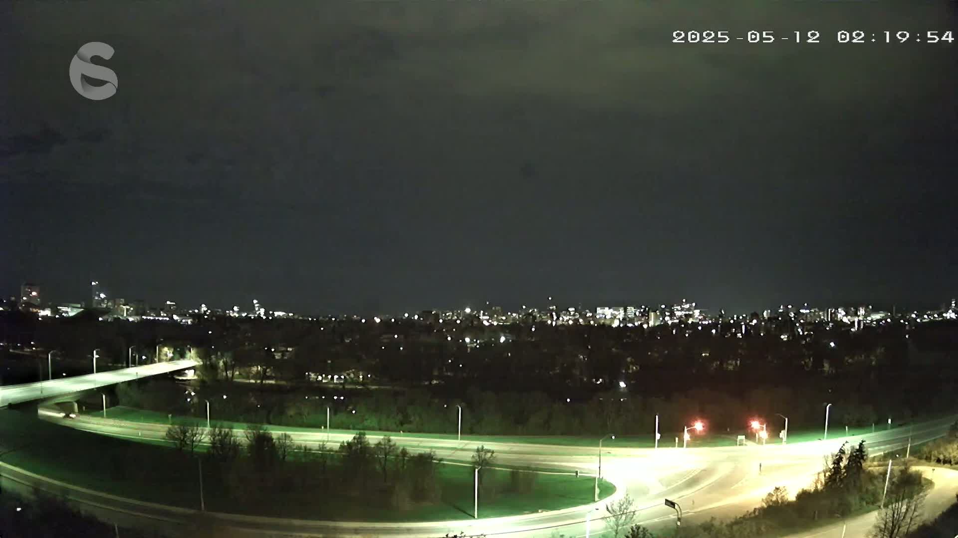 A nighttime view of a city skyline across a highway interchange under a mostly clear sky.