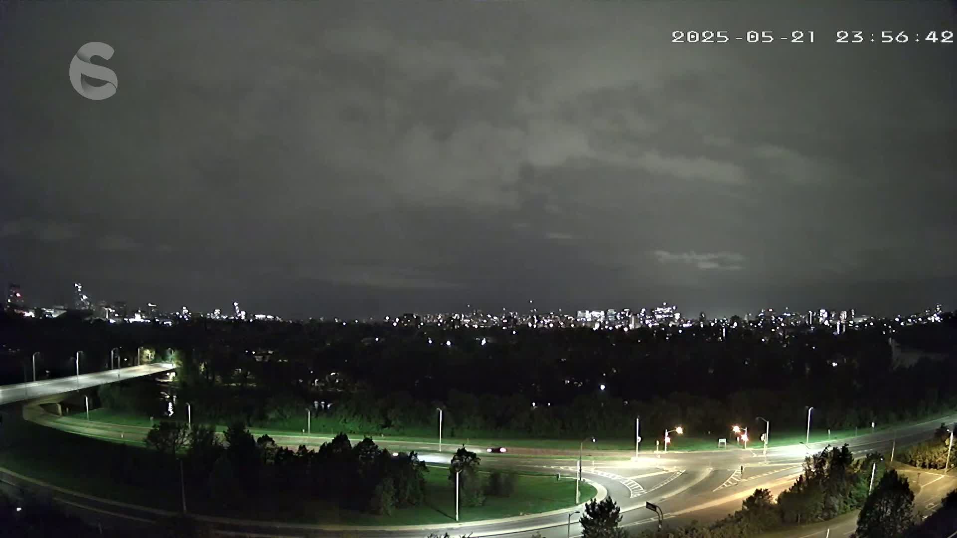 A nighttime, overcast view of a highway interchange and a distant city skyline.