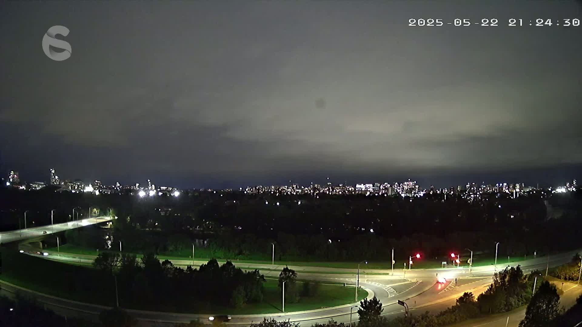 A nighttime view of a city skyline across a highway interchange under an overcast sky.