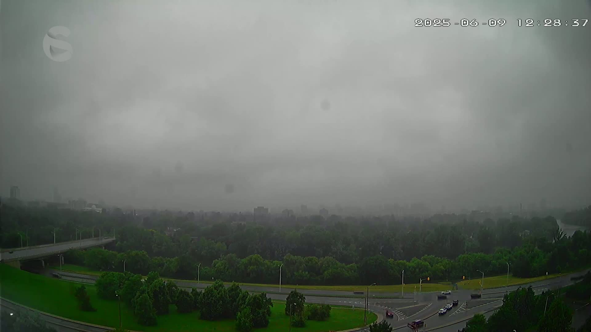 A highway curves through a lush green landscape under a heavy, overcast sky.