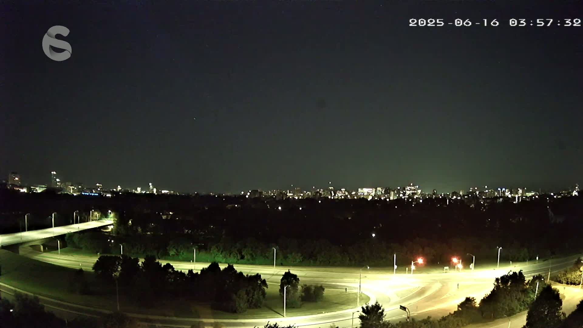 A nighttime view of a highway interchange with a city skyline in the distance under a clear sky.