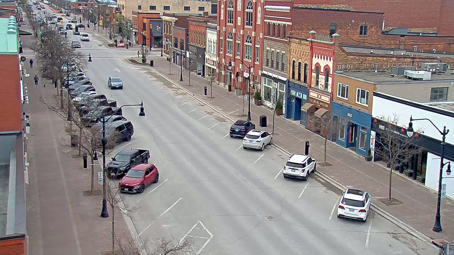 A mostly empty street lined with brick buildings and parked cars on a cloudy day.