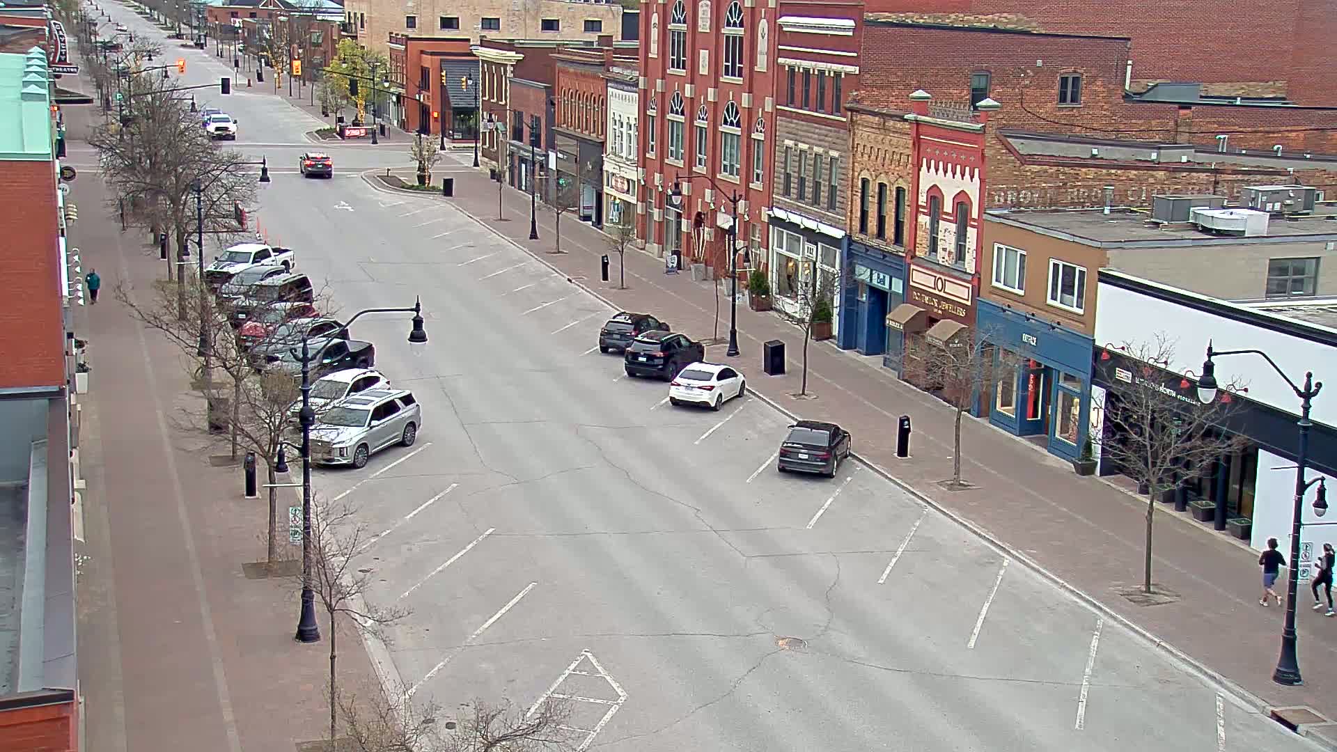 A mostly empty street lined with brick buildings on a partly sunny day, with a few cars parked along the sides.