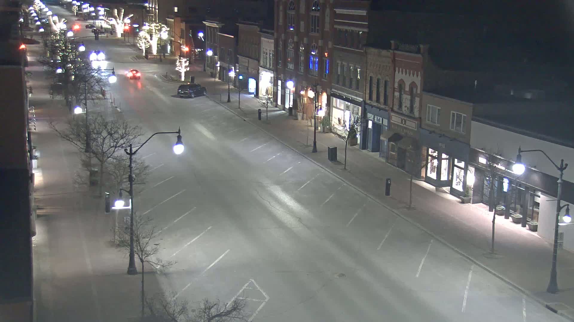 A mostly empty street at night lined with shops and bare trees, illuminated by streetlights.