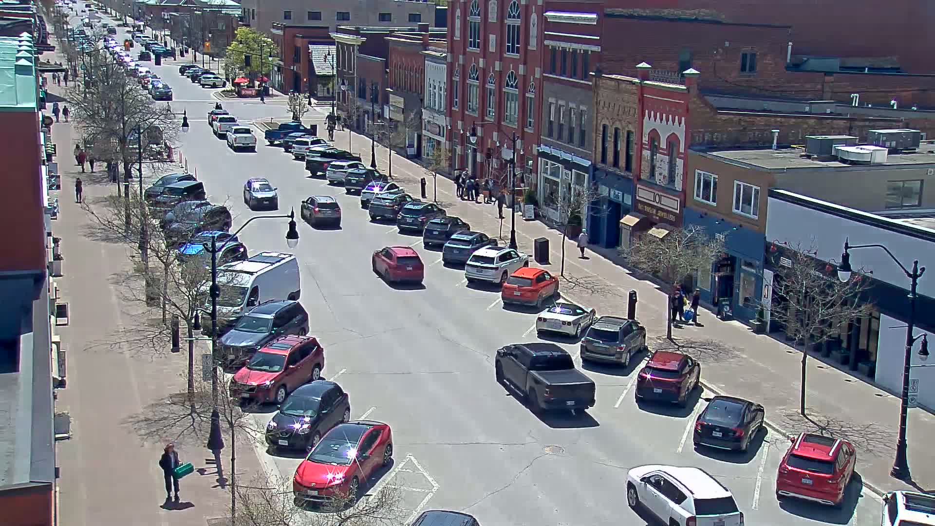 A street lined with parked cars and shops on a sunny day.