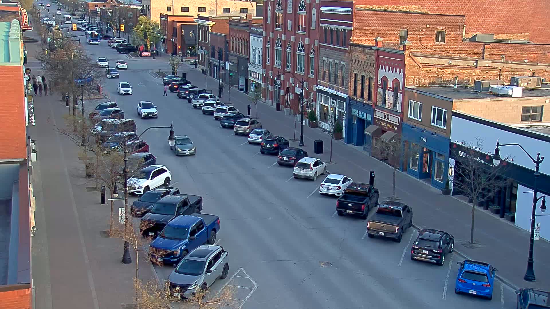 Cars are parked along a city street lined with brick buildings under a partly sunny sky.