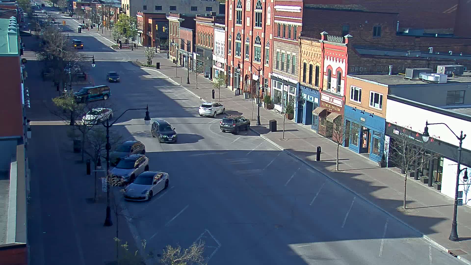 A mostly sunny, sparsely populated street lined with brick buildings and several parked cars.