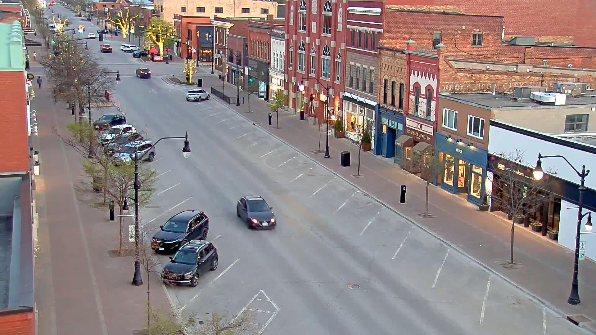 A mostly empty street lined with brick buildings and parked cars, under a dusky sky.