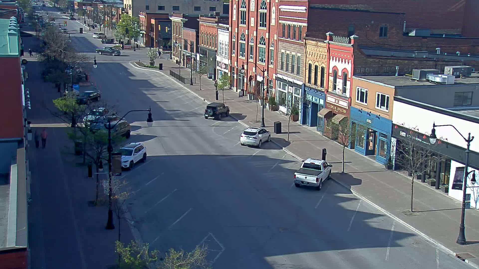 A mostly empty street lined with brick buildings and parked cars on a sunny day.