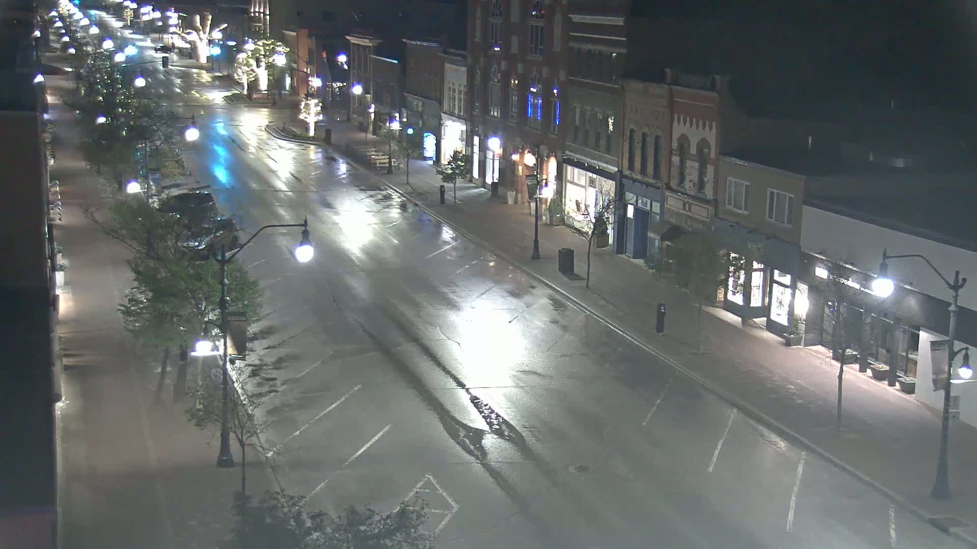 A wet, empty street at night lined with two-story buildings and streetlights.