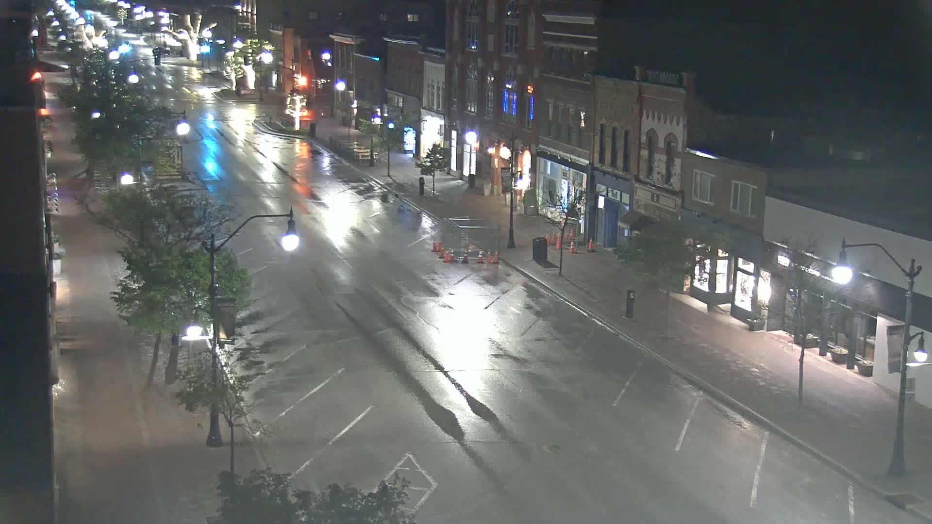 A wet, empty street at night lined with buildings and streetlights.
