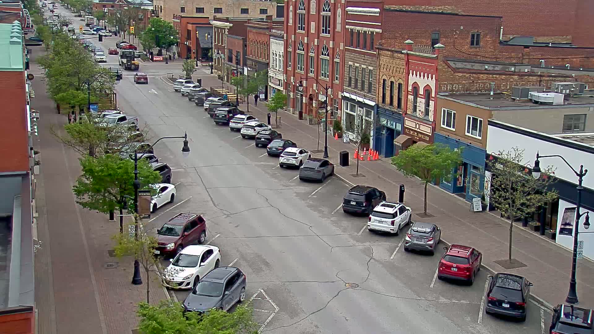 A street lined with parked cars and brick buildings, under a partly cloudy sky.