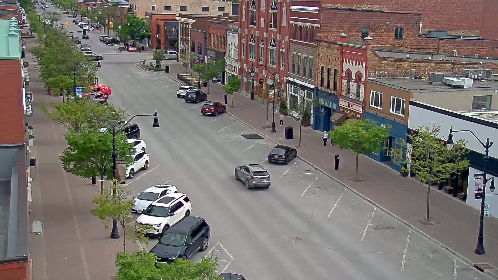A mostly empty street lined with brick buildings and parked cars on a partly sunny day.
