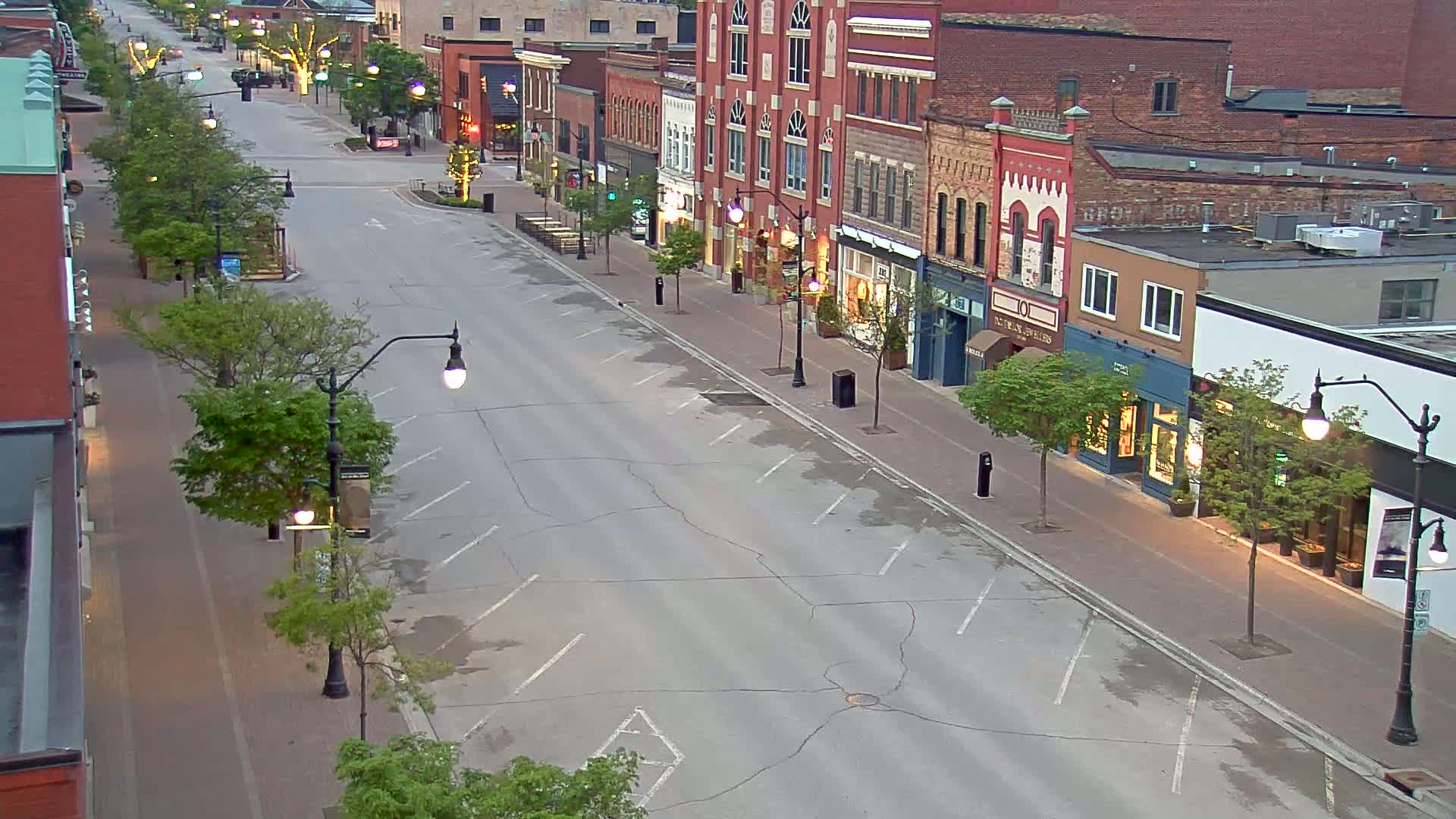 A mostly empty street lined with brick buildings and young trees, under a twilight sky.