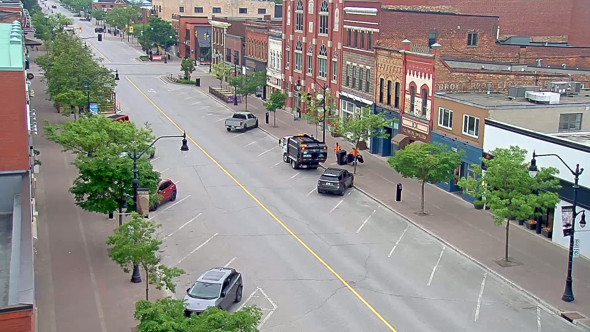 A mostly empty street lined with brick buildings and parked cars under a partly sunny sky.