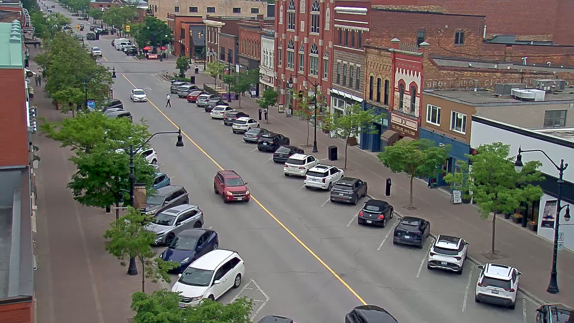 Cars are parked on both sides of a street lined with brick buildings on a partly cloudy day.
